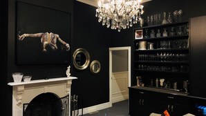 Una sala de estar con chimenea, candelabro, un cuadro grande y una estantería llena de cristalería.