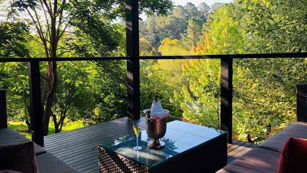 Un área de estar moderna al aire libre con una mesa de vidrio, una copa de vino y un vaso de cobre.