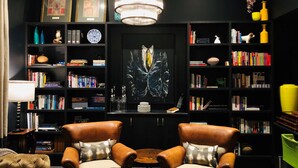 Una sala de estar moderna con sillones de cuero, un cuadro central y una estantería llena de libros y objetos decorativos.