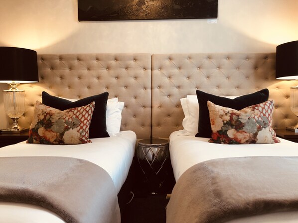 A hotel room with a mirrored wall, two beds with matching headboards, white linens, and decorative pillows.