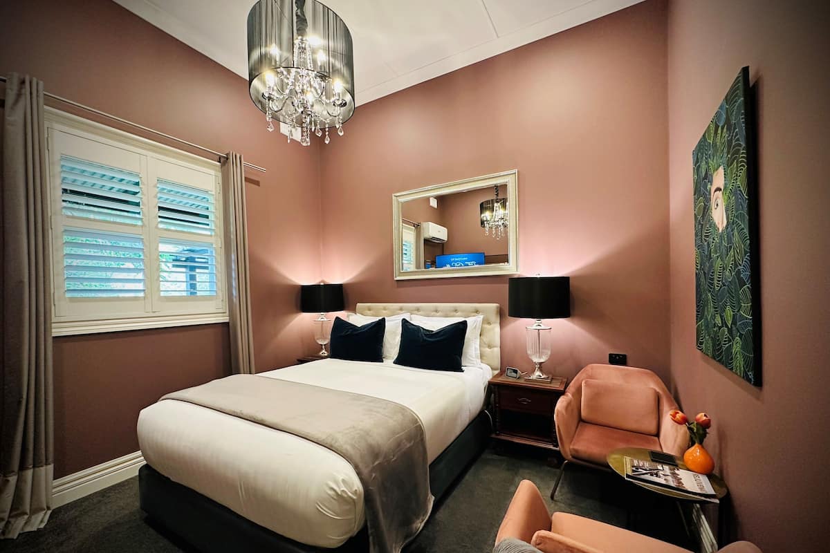 A hotel room with a bed, bedside lamps, a chair, a mirror, and a painting on the wall.