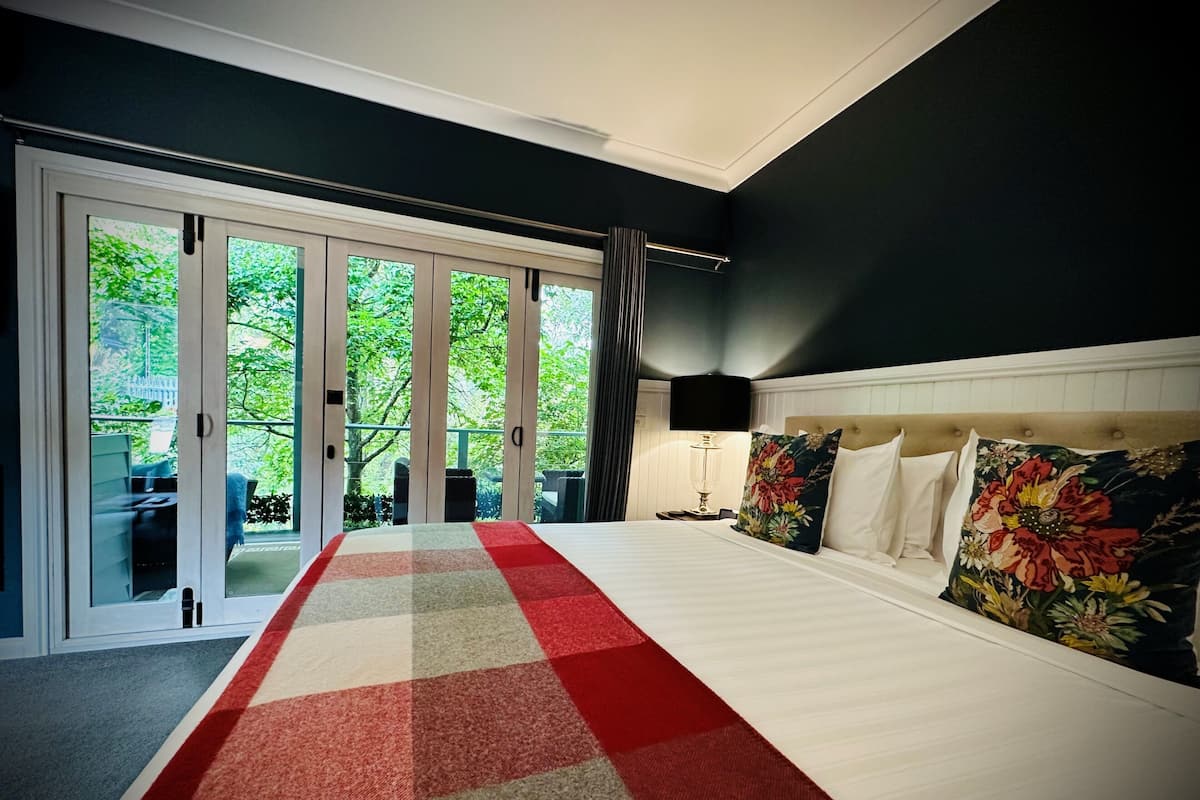 A bedroom with a large bed, a nightstand, a lamp, and a view through glass doors to an outdoor area.