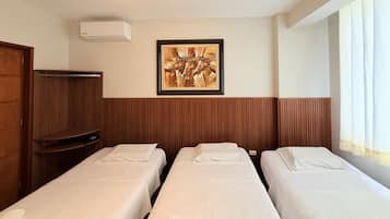 A hotel room with two single beds, a wooden wardrobe, a framed artwork on the wall, and a window with curtains.