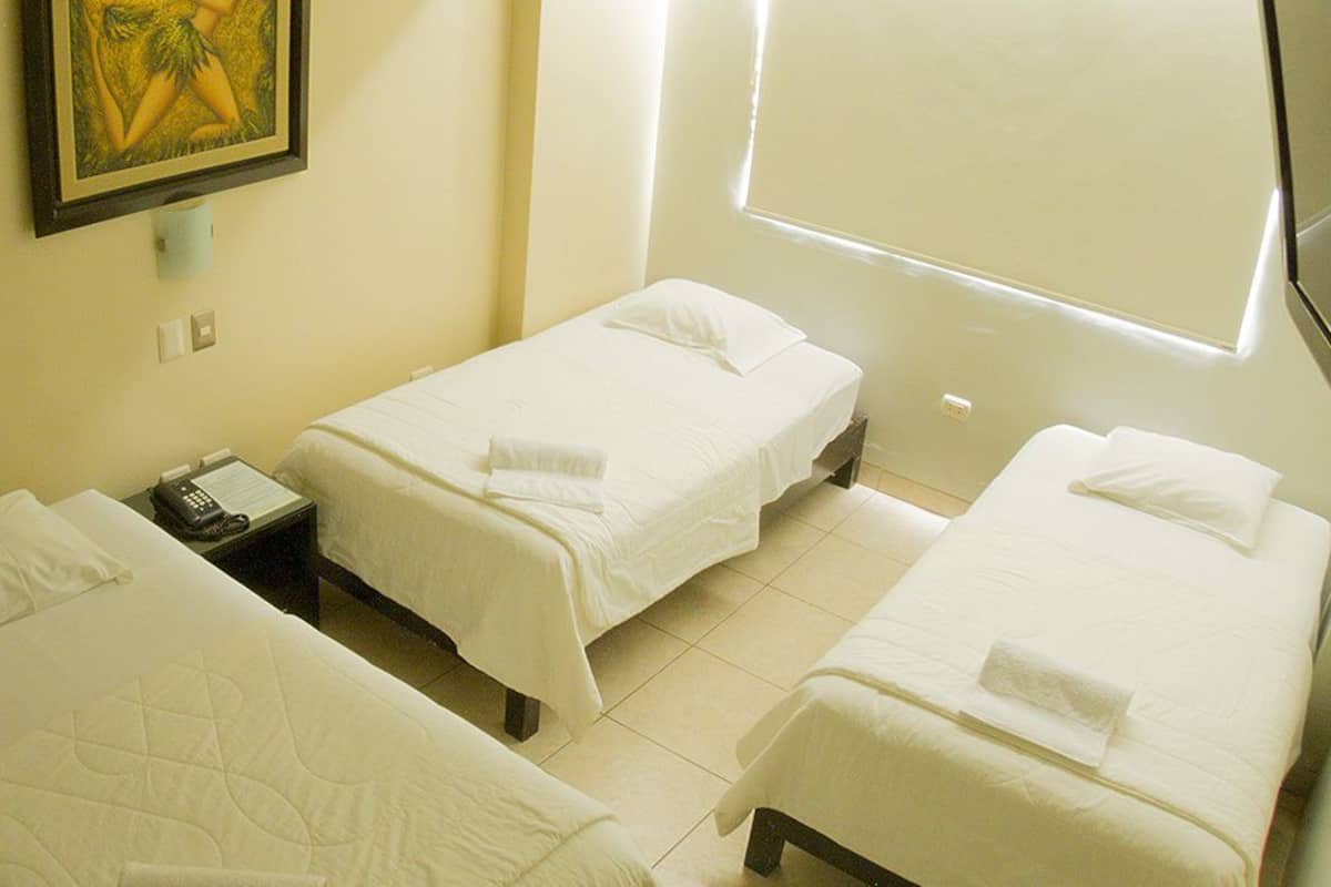 A hotel room with two single beds, a bedside table with a telephone, and a window with blinds.