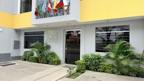 Entrada de un hotel con un cartel que dice 'RIVERA DEL RIO HOTEL', una puerta de vidrio y un pequeño jardín con plantas.