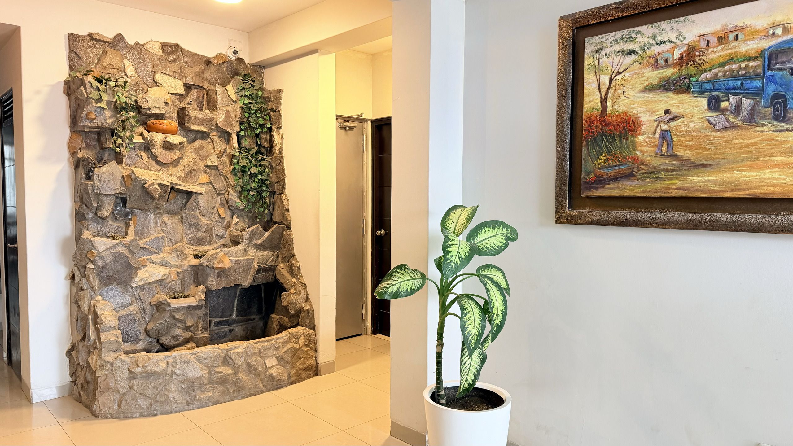 Paredes de pedra com lareira embutida, um vaso com planta de folhas coloridas e um quadro na parede.