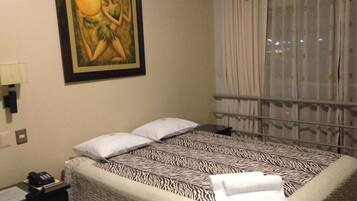 Habitación de hotel con cubrecama estampado con diseño de cebra, un cuadro en la pared y una ventana con cortinas.