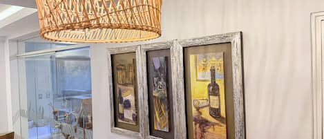 Un pasillo con tres obras de arte enmarcadas en la pared, una lámpara de techo de mimbre y una puerta de cristal que da a un comedor.