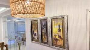 A hallway with three framed artworks on the wall, a wicker chandelier, and a glass door leading to a dining area. - Rivera del Rio Hotel (Piura)