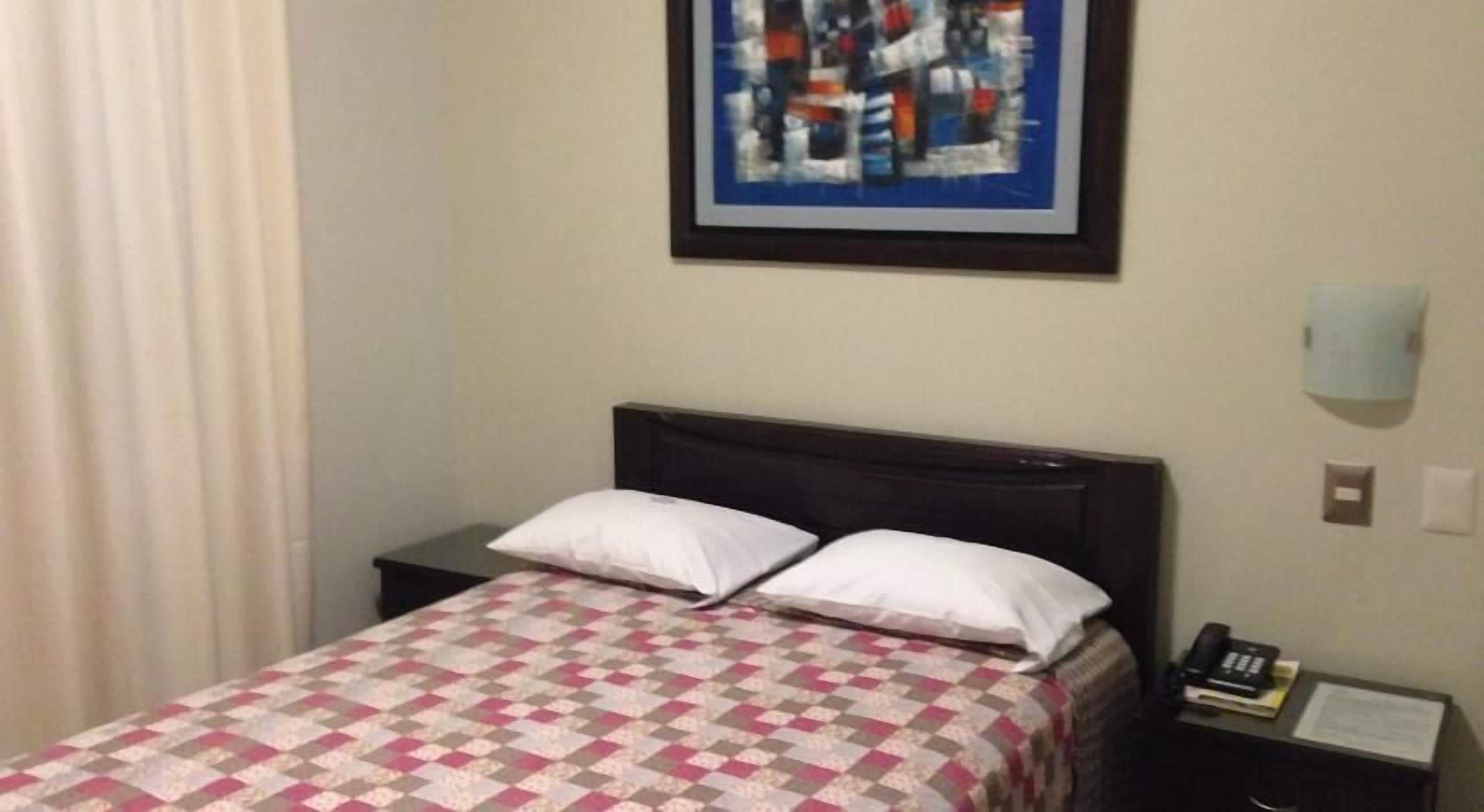 A hotel room with a bed, a nightstand, a telephone, and a framed abstract painting on the wall.
