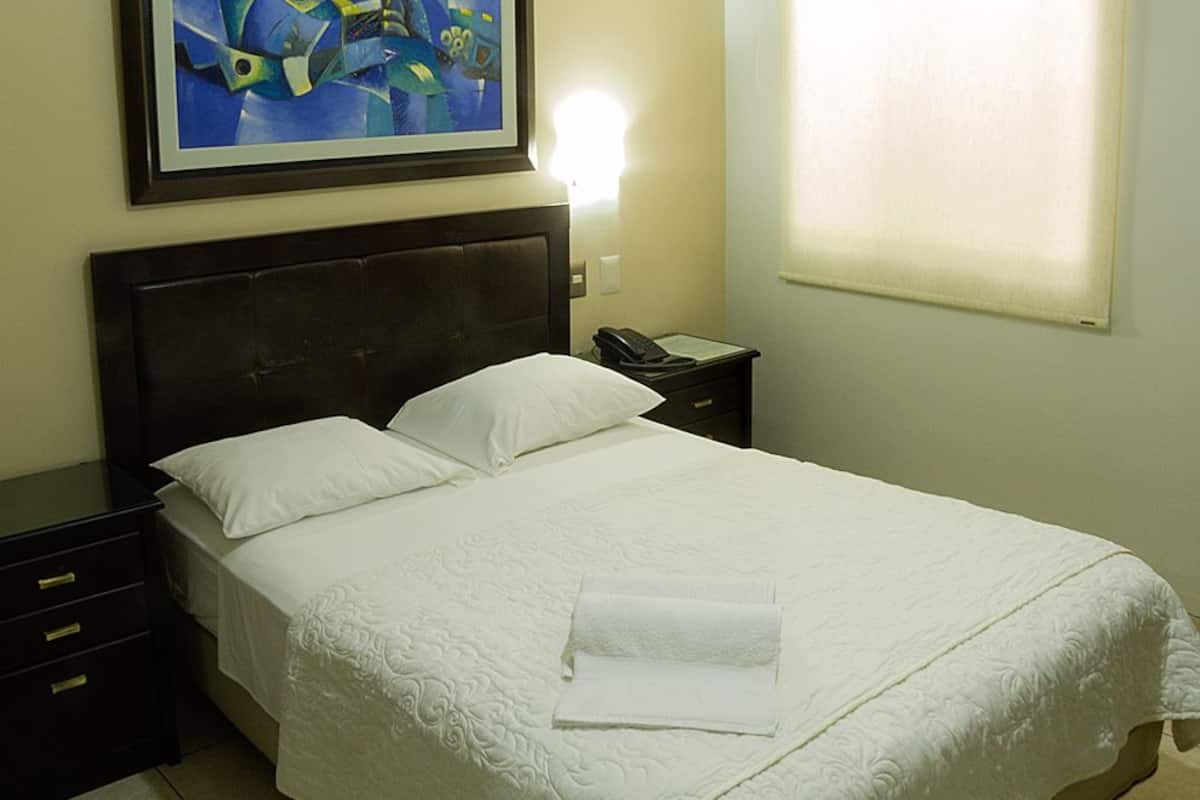 A neatly made bed with white linens, a dark headboard, a bedside table with a phone, and a painting on the wall.
