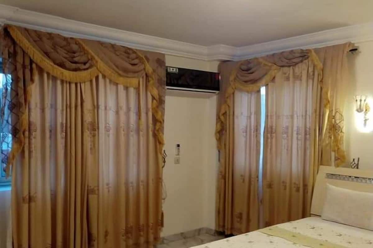 A bedroom with a bed, curtains, a ceiling light, and a wall-mounted air conditioning unit.