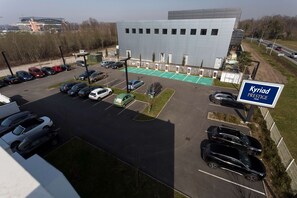 Een parkeerplaats met meerdere auto's, een bord met de tekst 'Kyriad Prestige Hotel' en een modern gebouw op de achtergrond.