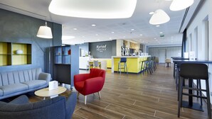 A modern hotel lobby with seating areas, a reception desk, and a bar.