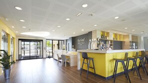A modern hotel lobby with a central bar area, seating, and a reception desk.