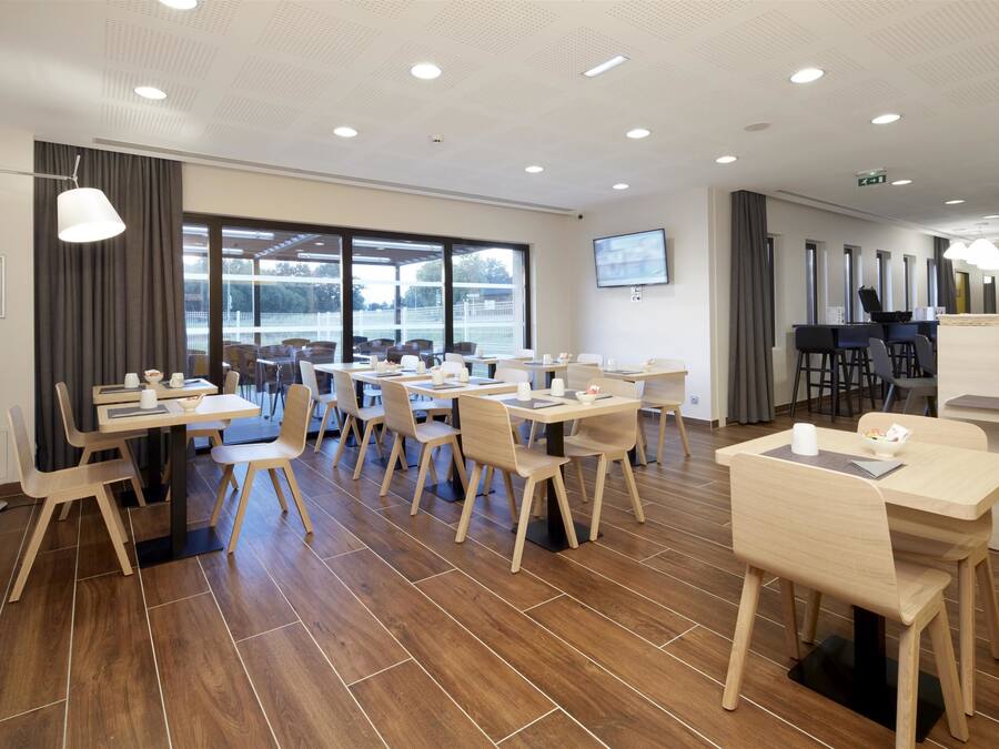 A modern conference room with multiple tables and chairs, large windows, and a flat-screen TV on the wall.