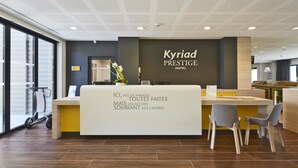 A reception desk at Kyriad Prestige Hotel with a modern design, a large window, and a wheelchair-accessible area.