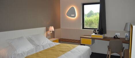 A hotel room with a bed, a desk, a chair, a window with a view, and a wall-mounted light.