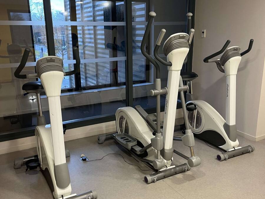Ein Fitnessraum mit Laufbändern und Crosstrainern, großen Fenstern und Blick auf die Stadt.