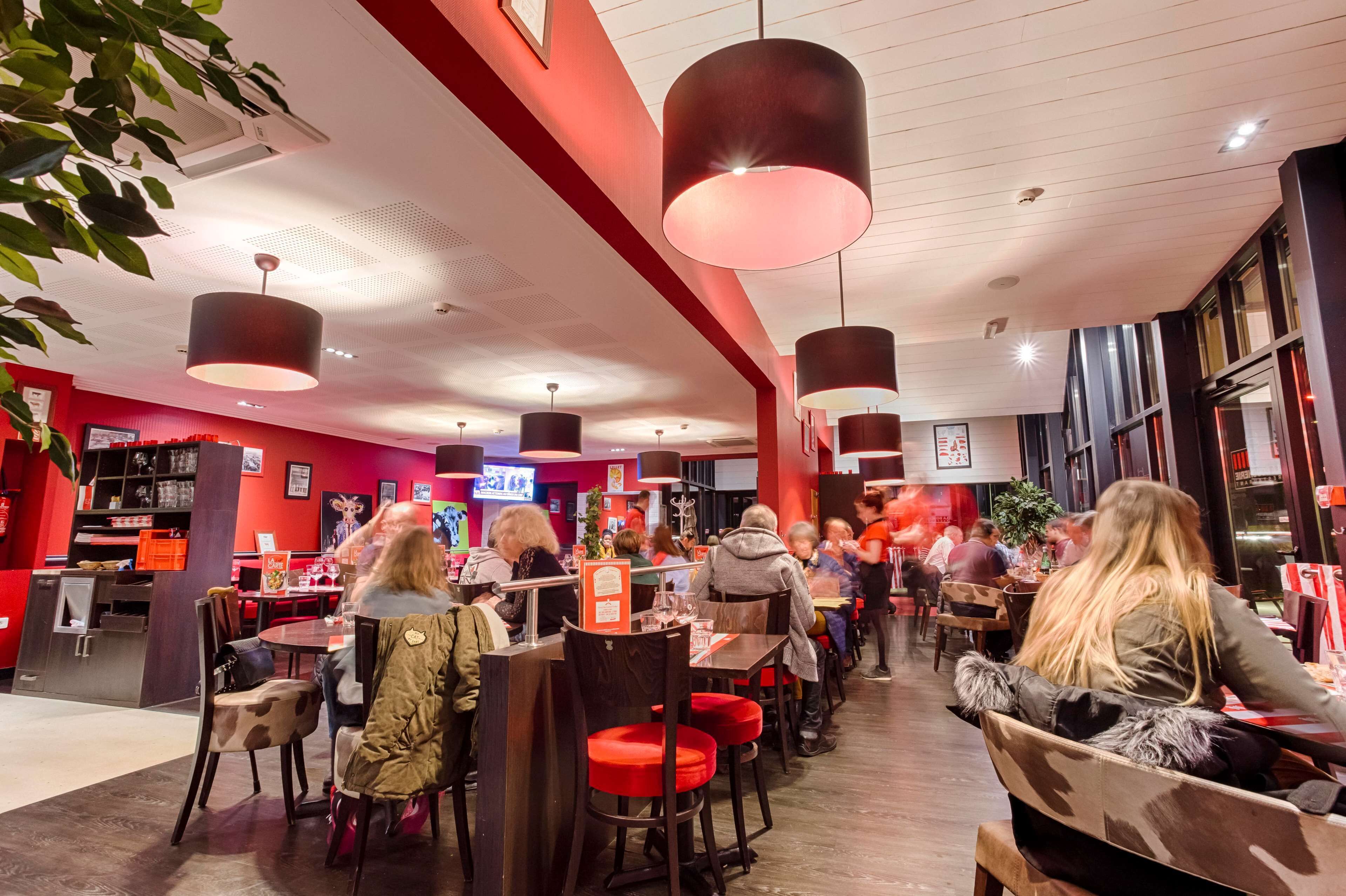 A restaurant with red walls, black and red chairs, and hanging pendant lights.