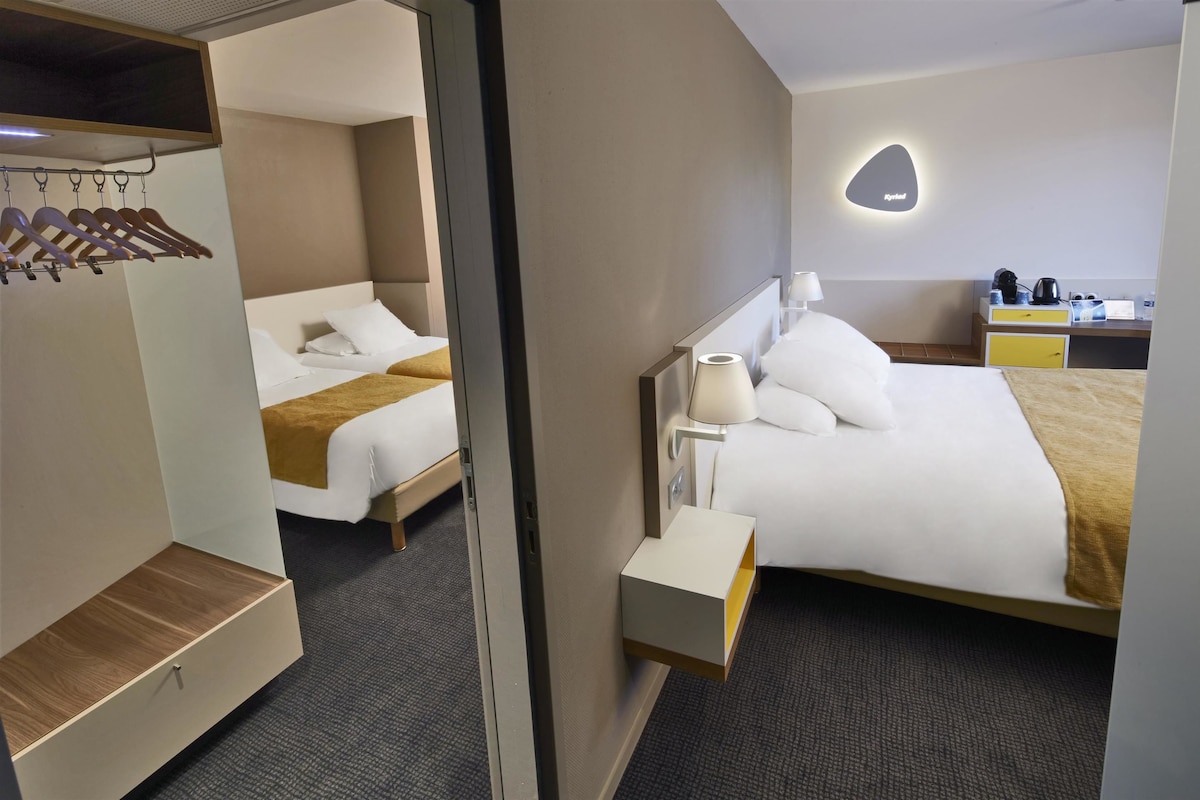 Een hotelkamer met een bed, nachtkastje, lamp en een klein bureau met stoel.