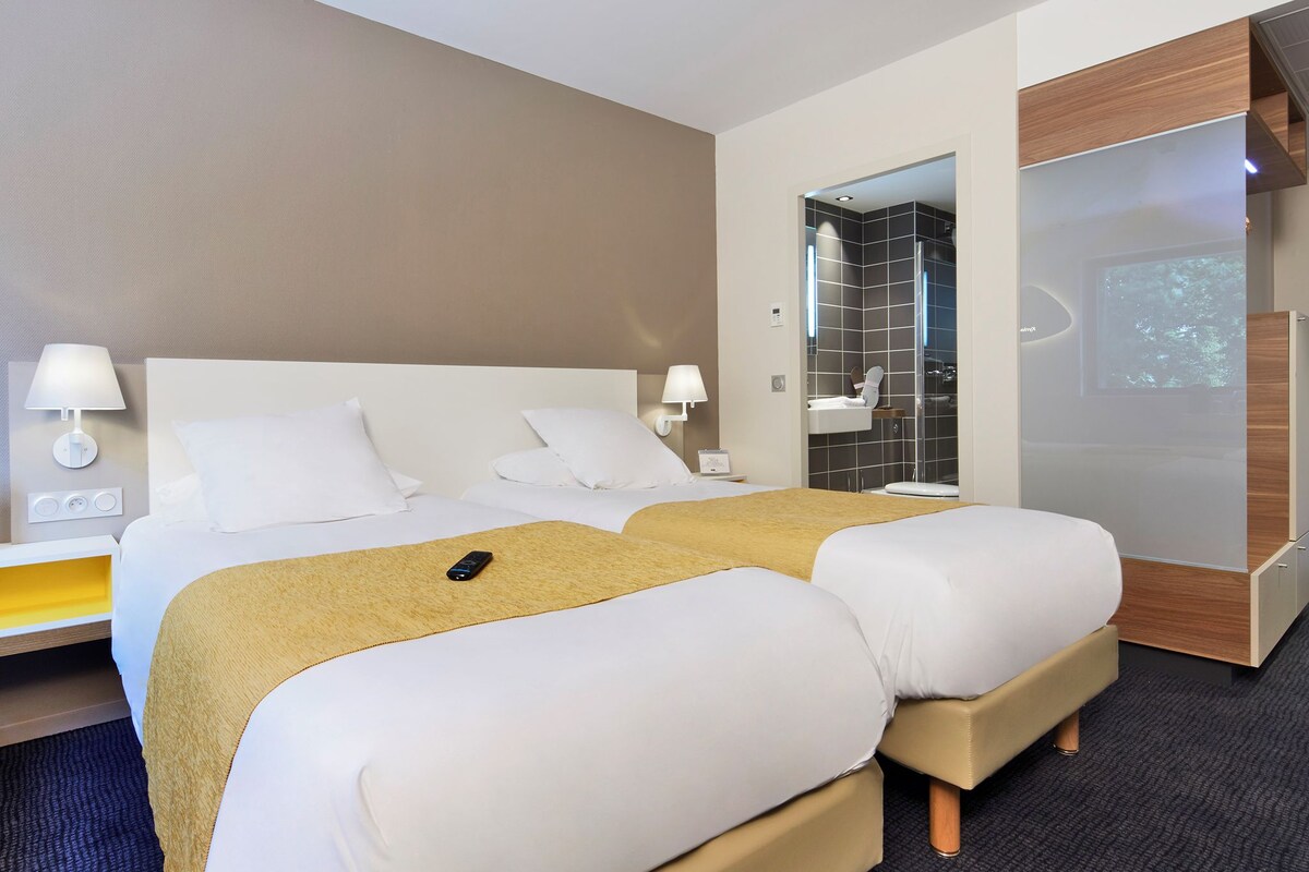 Hotelkamer met een groot bed, twee nachtkastjes, een badkamer met douche en een groot raam.
