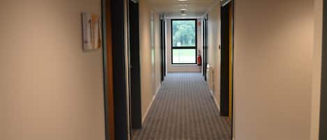 Ein Flur mit gemustertem Teppich, Türen an beiden Seiten und einem Fenster am Ende.