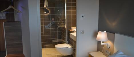 Un baño moderno con ducha, inodoro y una mesita de noche con lámpara.