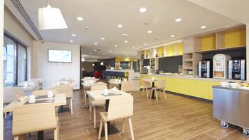 A modern dining area with wooden tables and chairs, a kitchen counter with appliances, and a bright ceiling with recessed lighting.