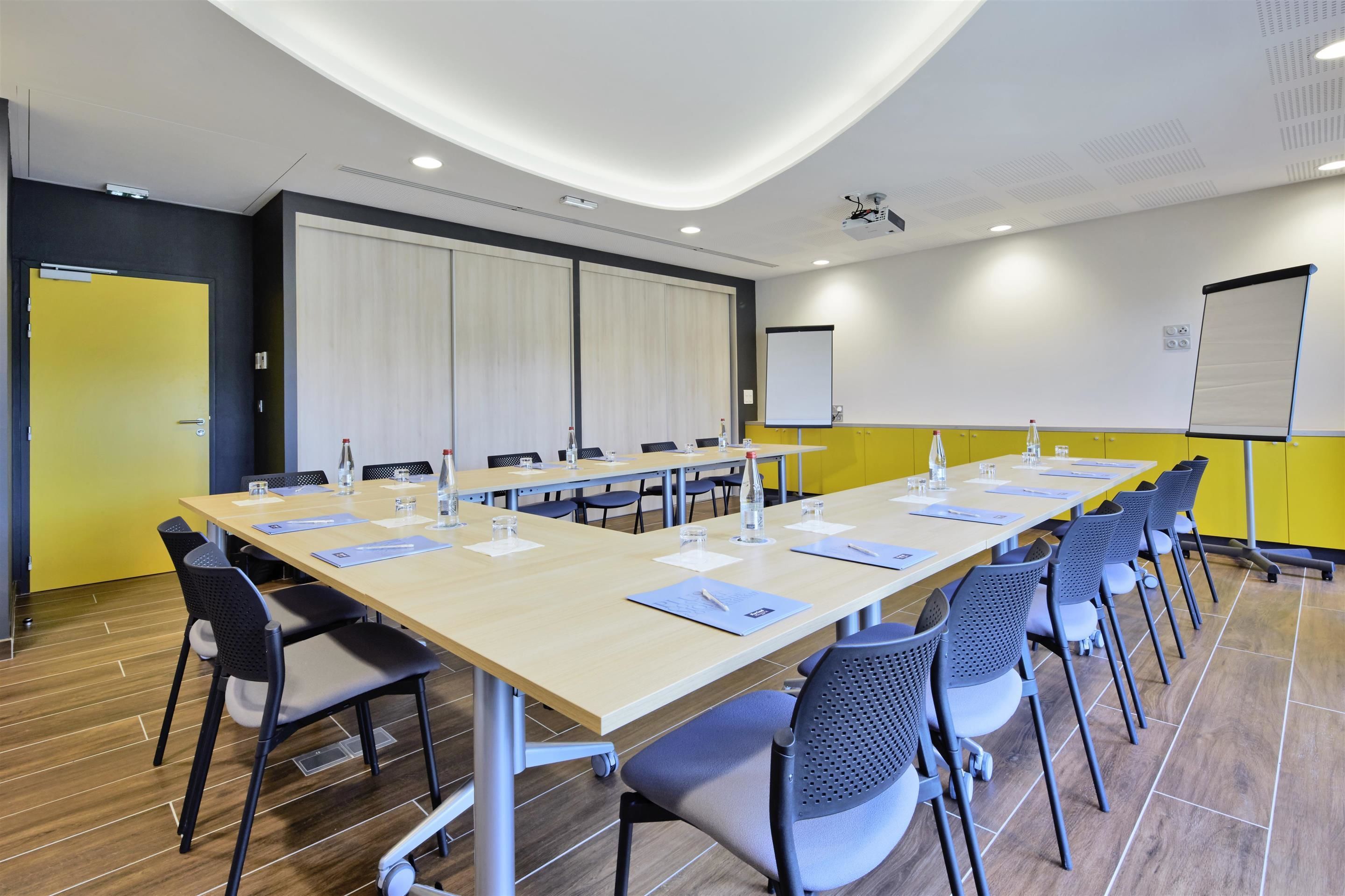 Ein Konferenzraum mit langem Tisch, Stühlen, einem Projektor und einer Tafel.