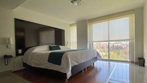 A modern hotel room with a large bed, a bedside table, a phone, and a window with a view of the outside.