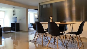 A modern living room with a dining area, a TV, and a large window with blinds.