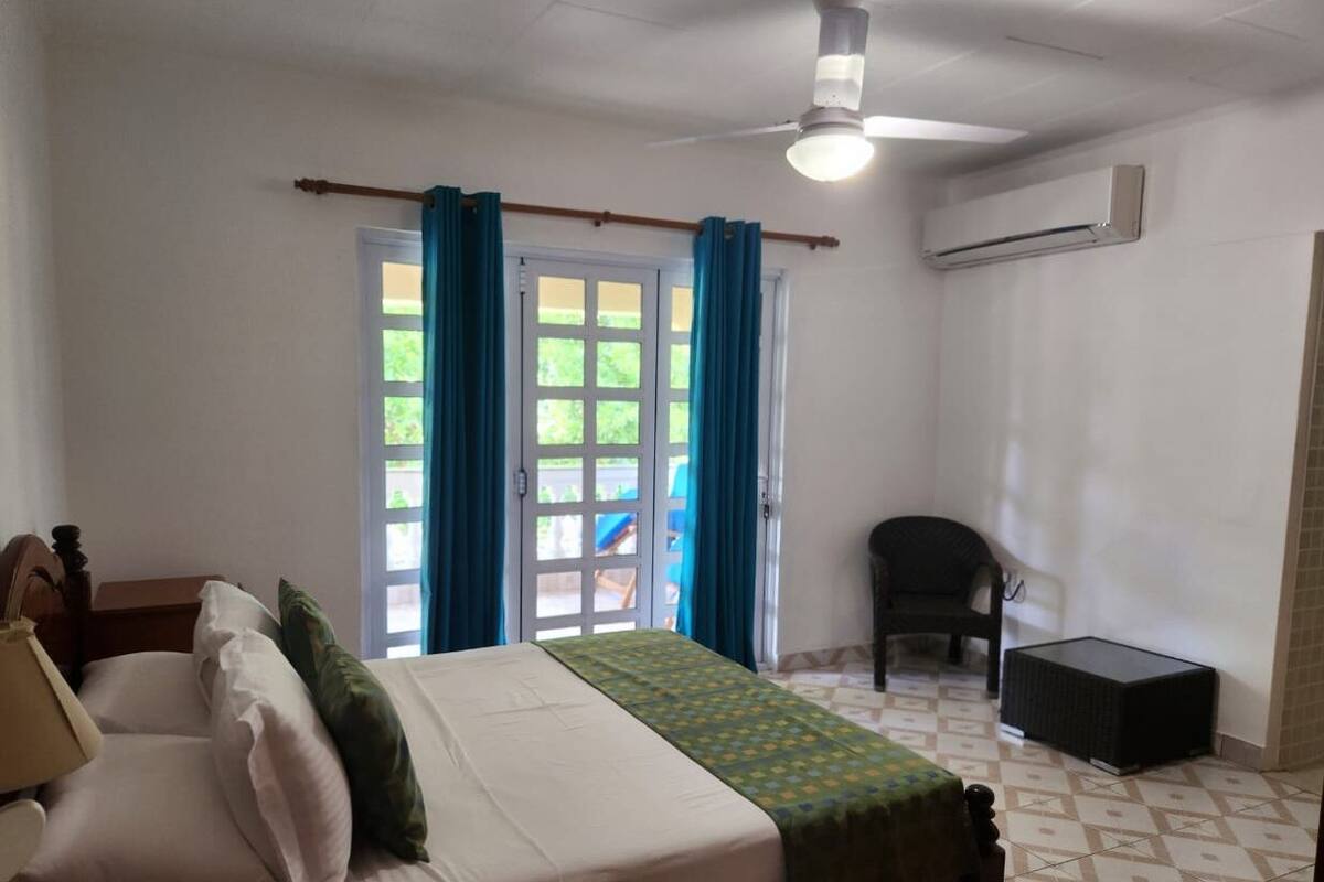 Une chambre à coucher comprenant un lit, une chaise, un appareil de climatisation et une fenêtre avec des rideaux.