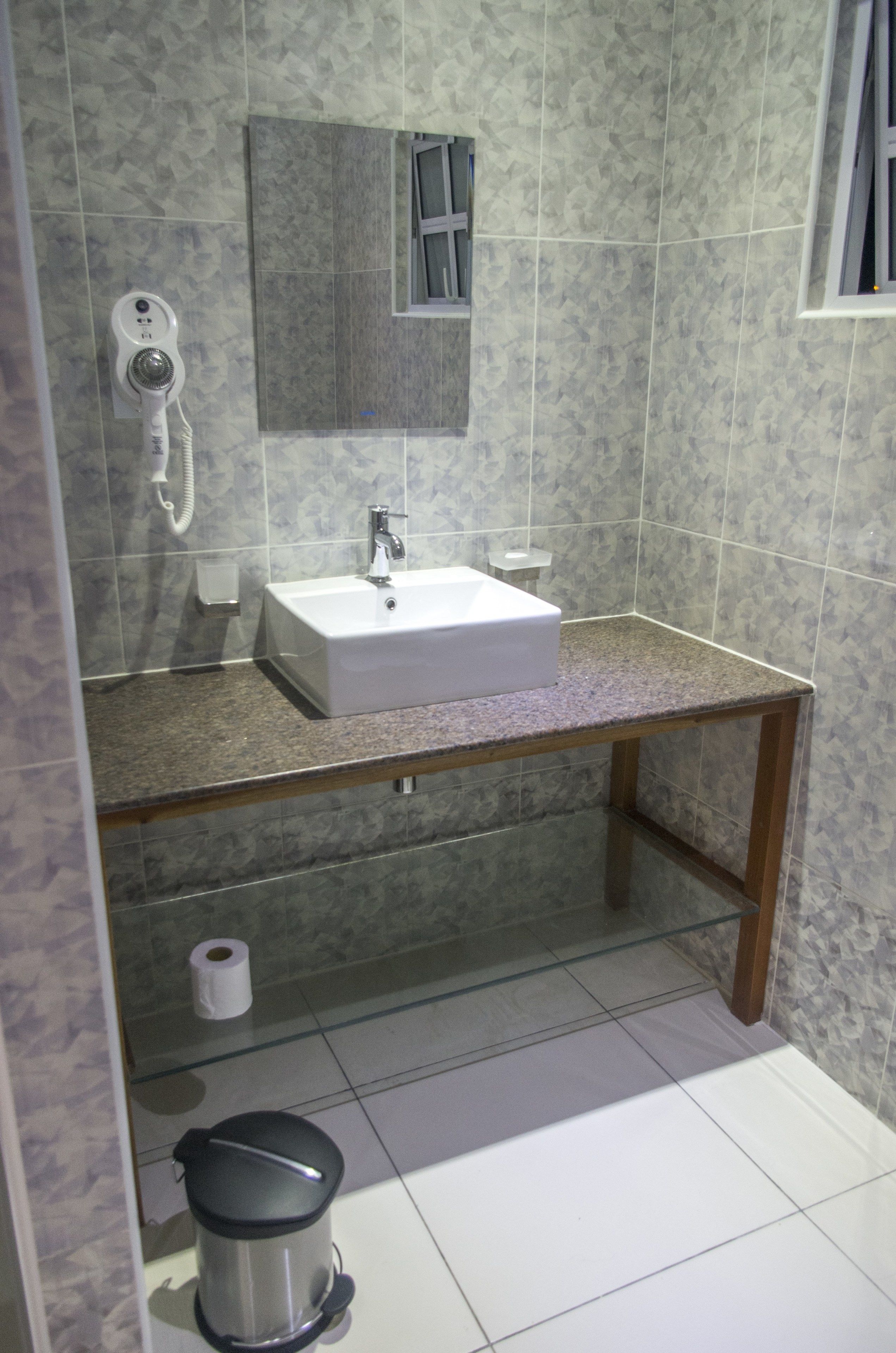 A bathroom with a sink, mirror, and a trash bin.