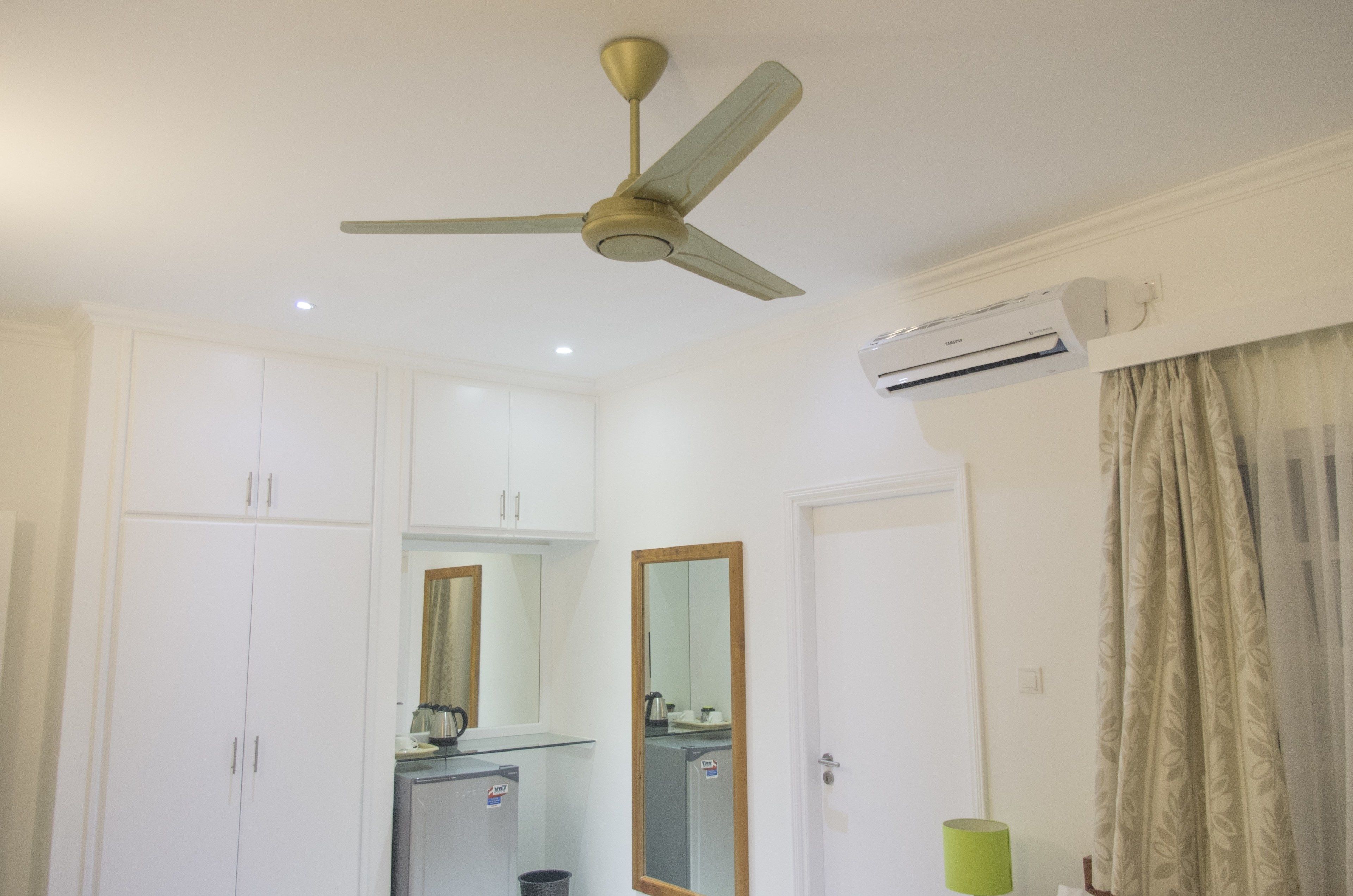 A room with a ceiling fan, white cabinets, a mirror, an air conditioning unit, and a green lamp.
