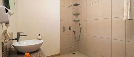 A bathroom with a white sink, a hairdryer, a glass shelf, and a shower area.