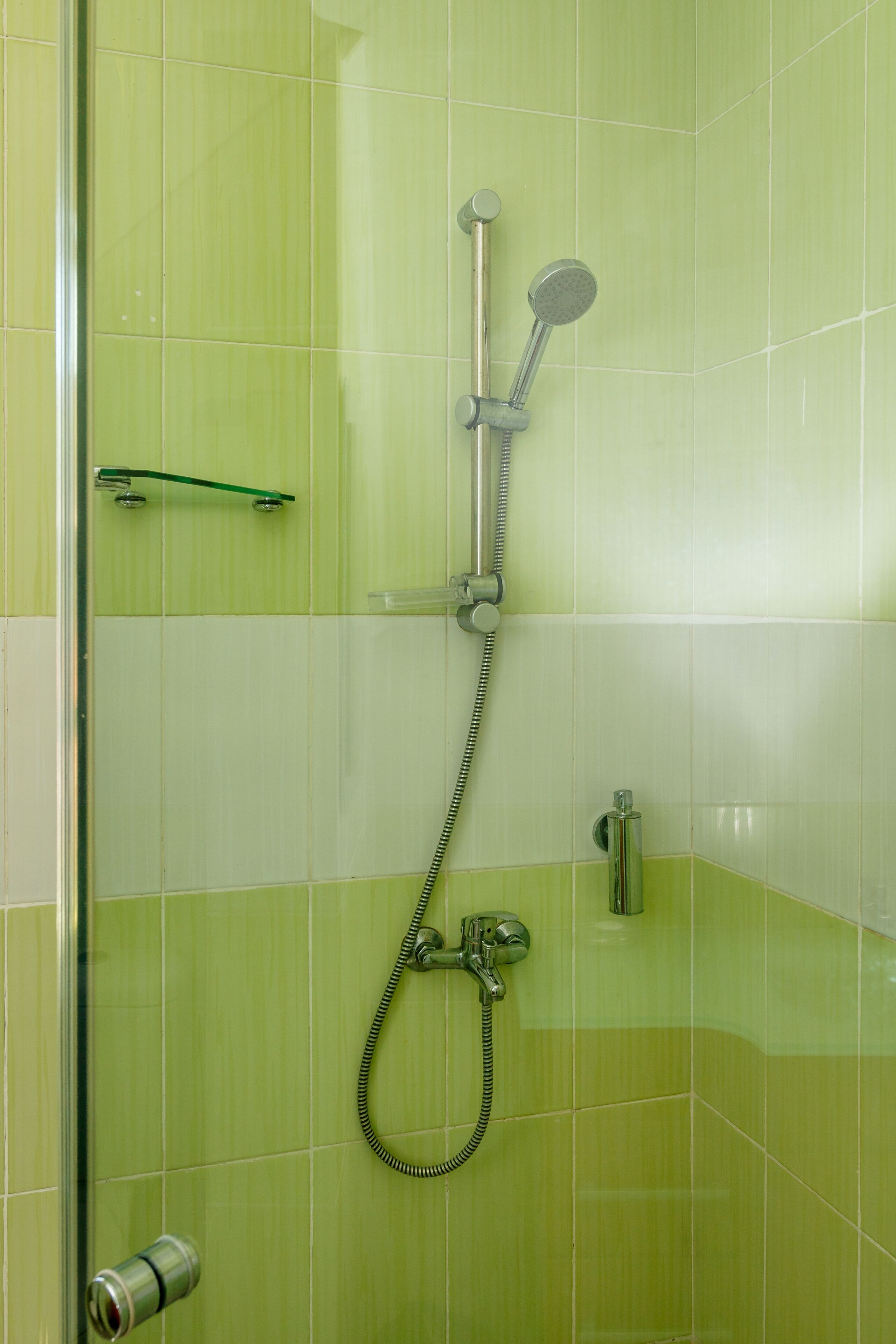A shower with a handheld showerhead and a wall-mounted faucet.