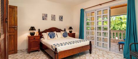Un dormitorio con cama, mesitas de noche, ventilador de techo y vista a través de un ventanal grande.