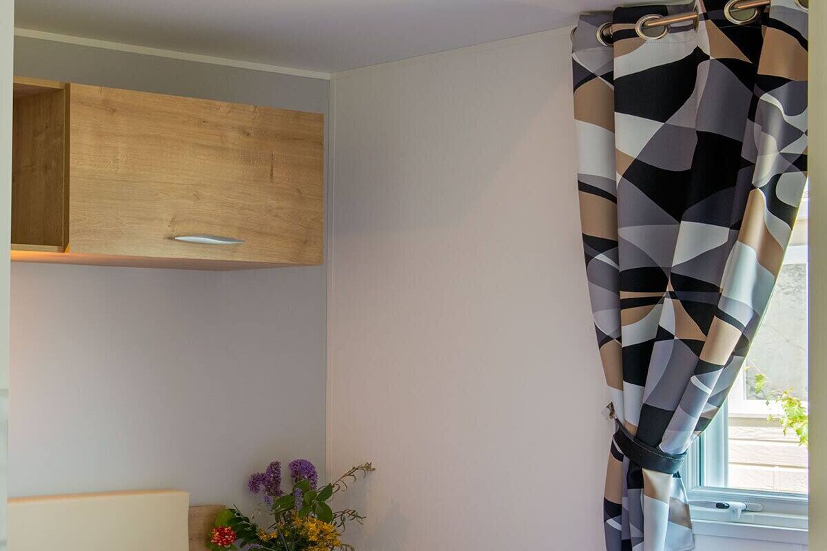 Un dormitorio con cama, un armario de madera, una ventana con cortinas y un jarrón con flores.