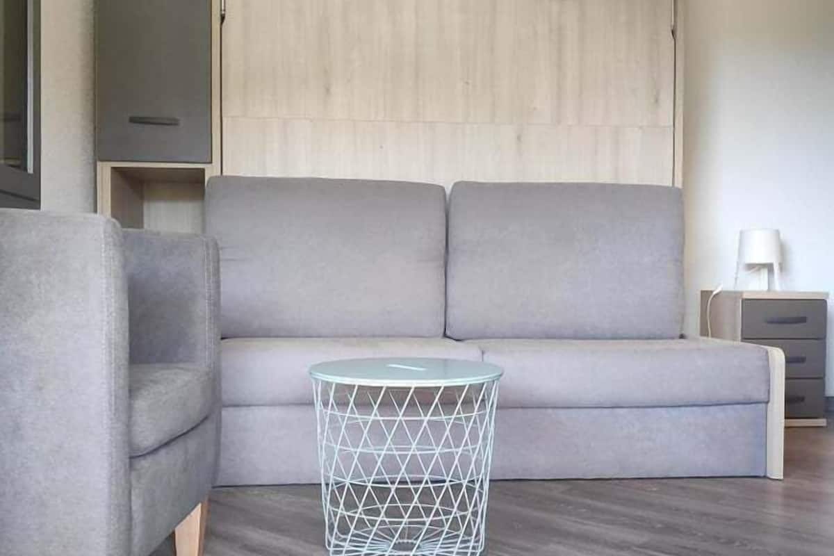 Una sala moderna con un sofá gris, una mesa de centro redonda de vidrio y una cesta blanca de alambre.