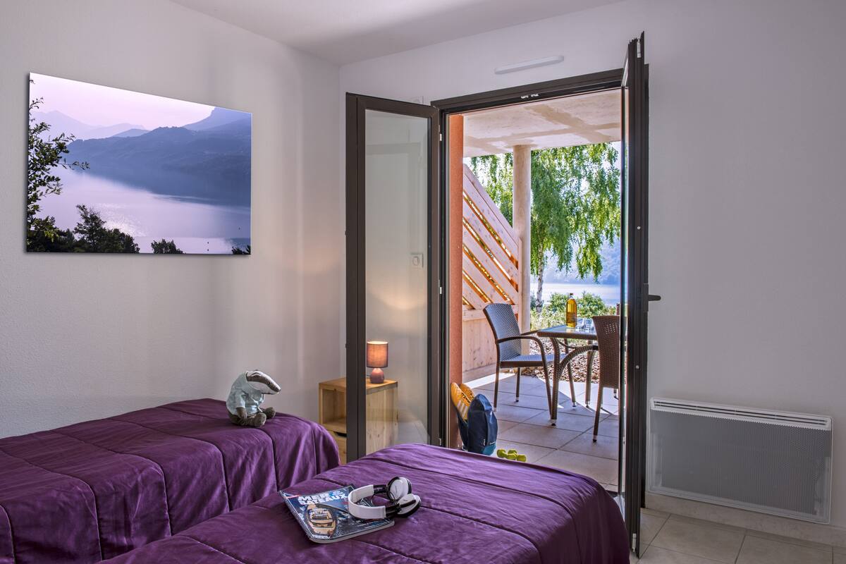 Una habitación con dos camas, vistas a un lago y un balcón con mobiliario exterior.