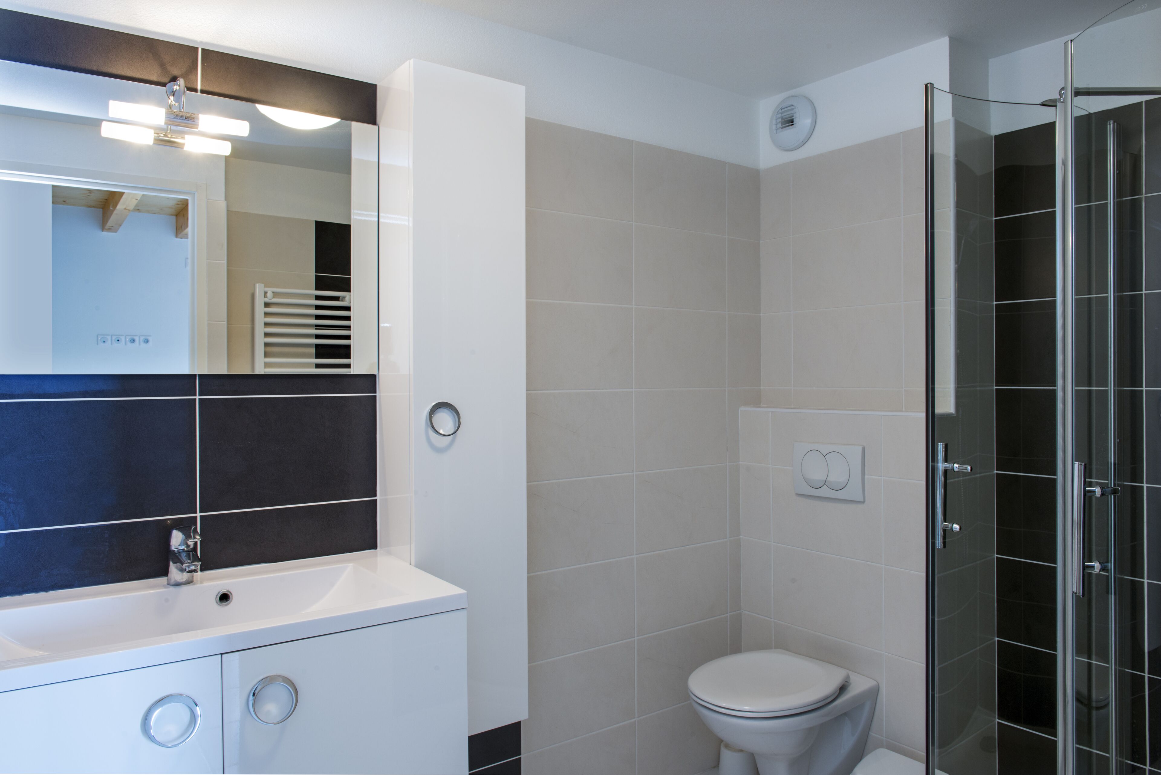 A modern bathroom with a white sink, mirror, and toilet. It includes a glass-enclosed shower area.