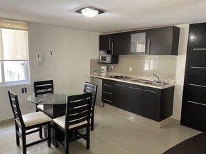 A compact kitchen with a round dining table, dark cabinets, and a built-in microwave.