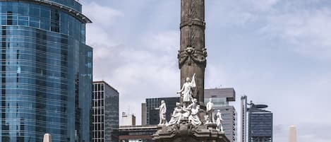 A tall monument with a golden angel statue, surrounded by a plaza with steps and people.