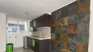 A modern kitchen with dark cabinets, a stainless steel sink, and a tiled backsplash. - Grupo Kings Suites Chimborazo (Mexico City)