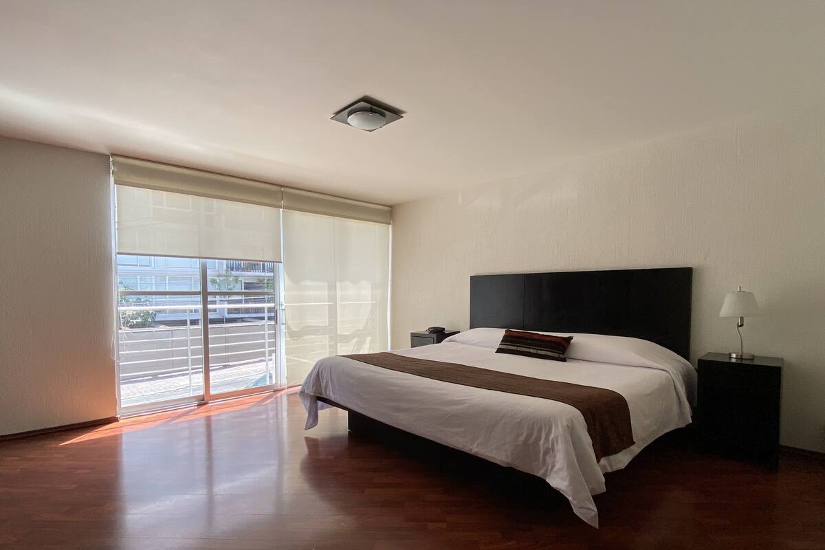 A modern bedroom with a large bed, a nightstand, a lamp, and a ceiling light.