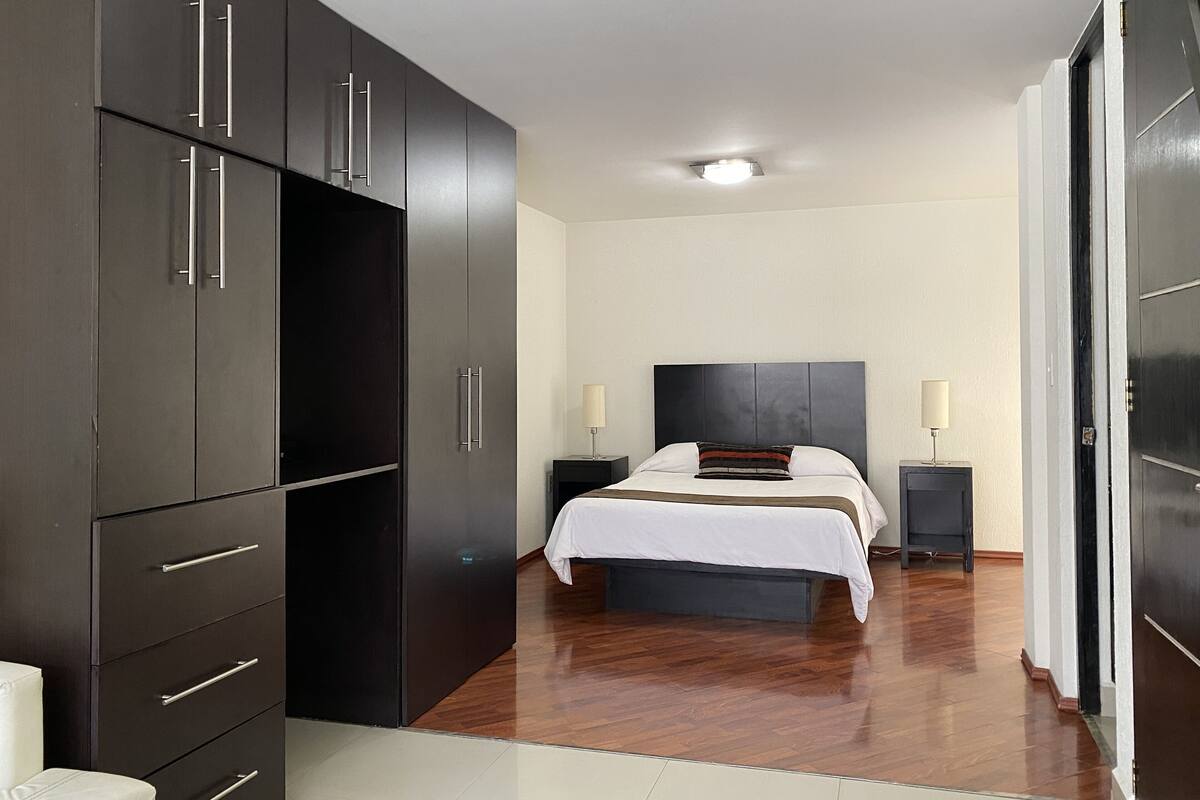 A modern bedroom with a large bed, built-in wardrobe, and bedside lamps.
