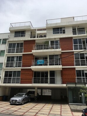 A multi-story building with balconies, a parking area, and a sign indicating a business or service.