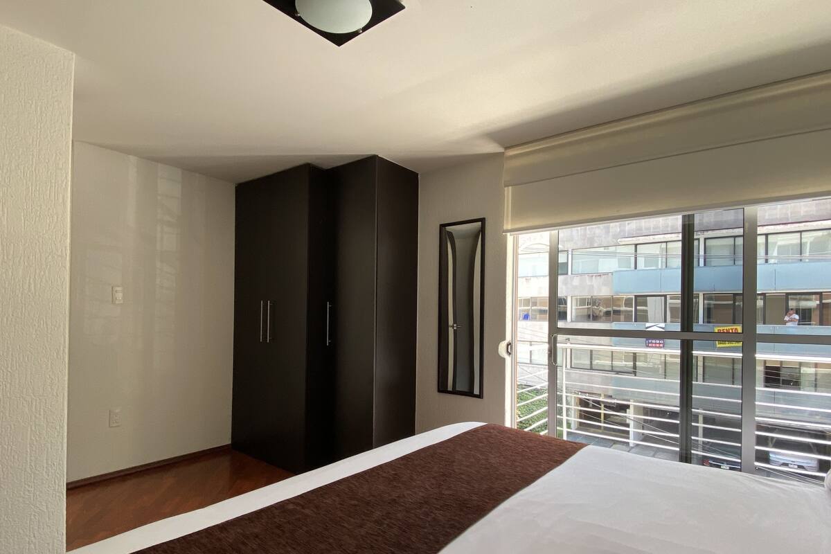 A bedroom with a large bed, a wardrobe, and a sliding glass door to a balcony.