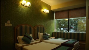 Habitación de hotel con dos camas, una ventana con vistas a árboles y luces fijadas a la pared.